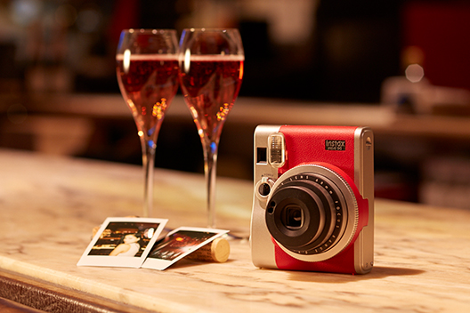 Red mini 90 camera with two photos and two drinks on table