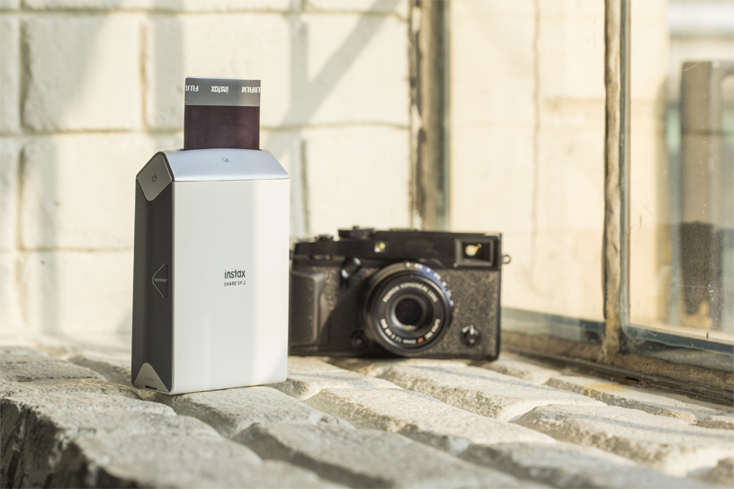 Silver SP-2 Printer next to black camera by the window