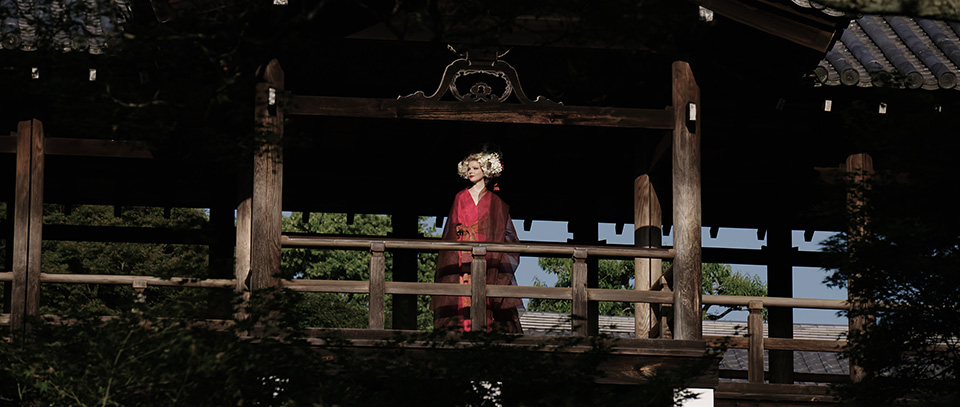 [photo] A more zoomed in wide shot of a lady in traditional Japanese attire standing under a tradional Japanese wooden house