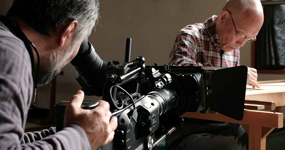 [photo] A cameraman looking through the viewfinder while filming a subject drawing with rulers
