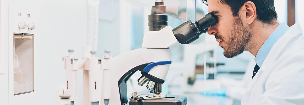 [image] Man in lab-coat looking through microscope in a laboratory