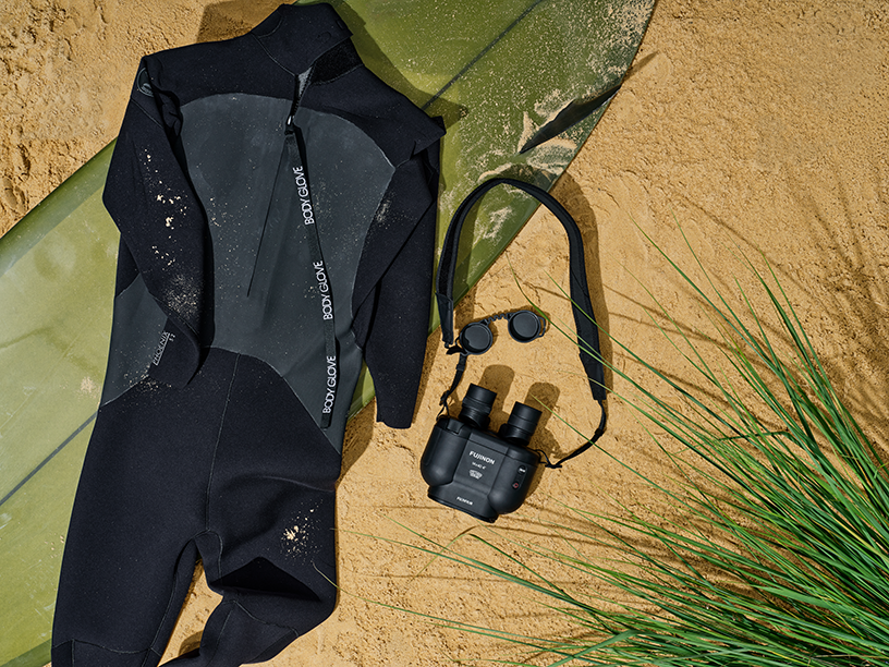 A wetsuit and binoculars placed on the sandy beach.